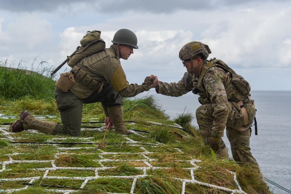 A World War II reenactor and a modern Ranger clasp hands on the Pointe du Hoc cliffs